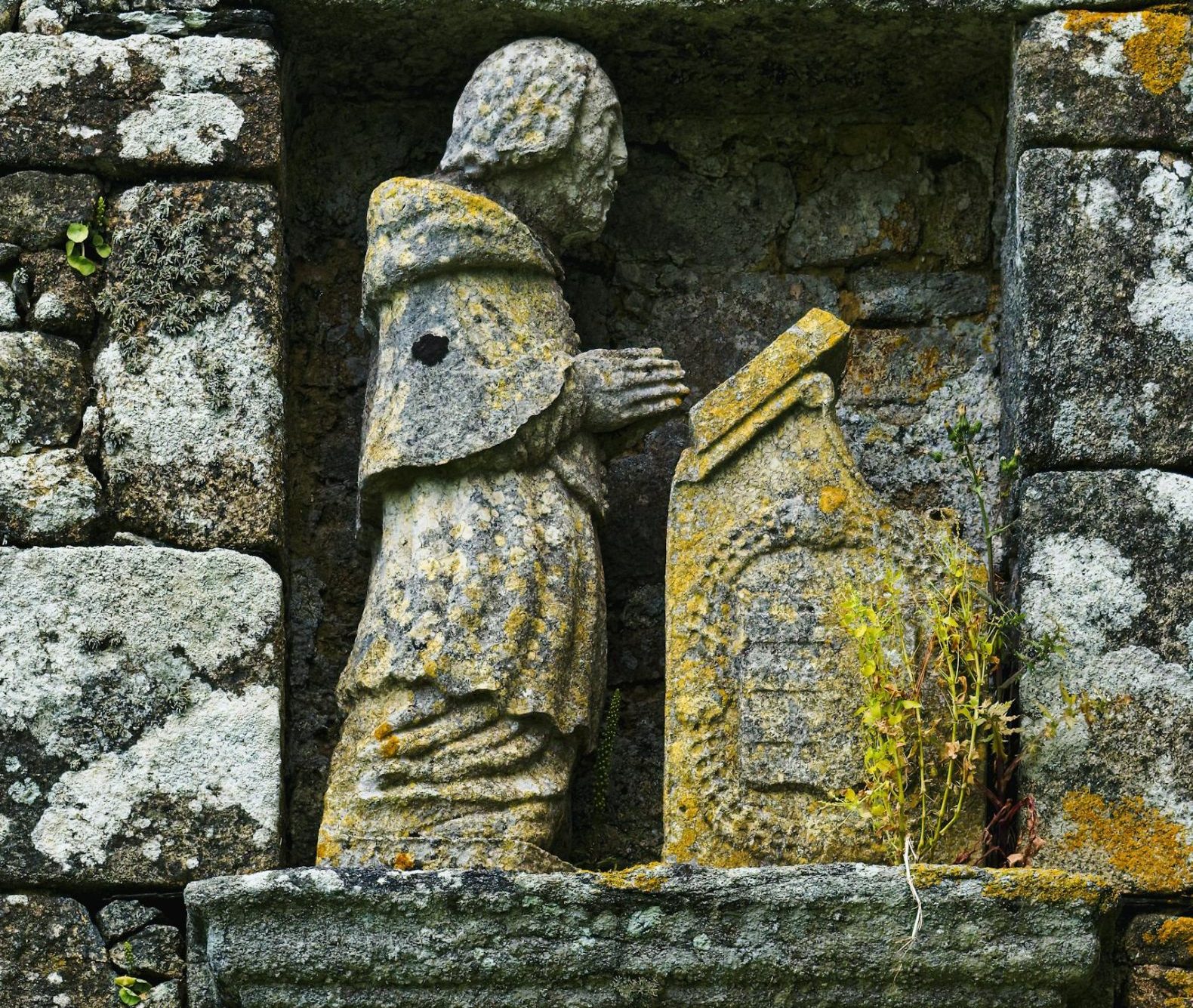 Praying stone statue set in a rustic wall in Saint-Pol-de-Léon, France.