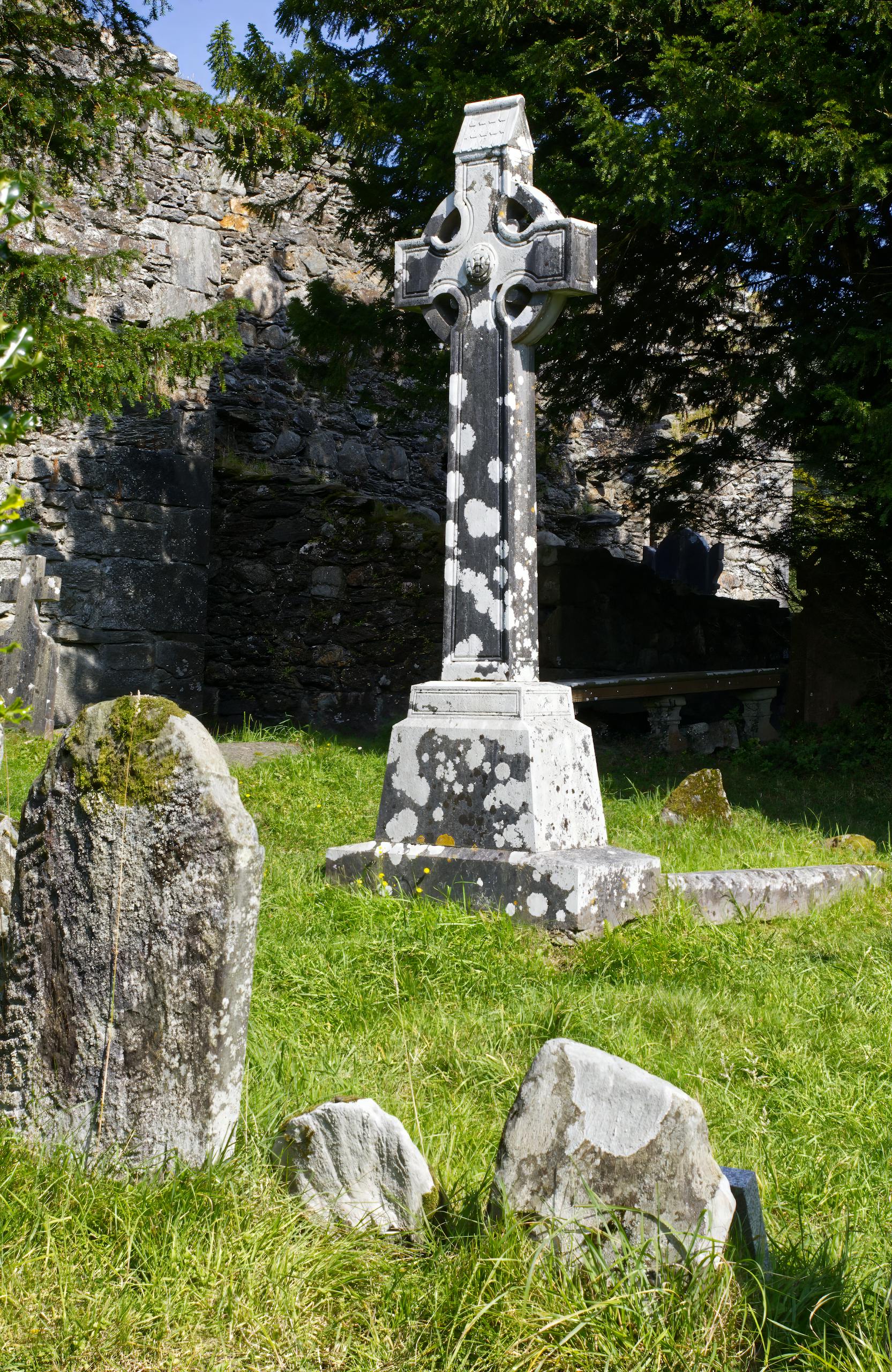 A Celtic cross stands amidst ancient headstones in a sunlit Wicklow graveyard.