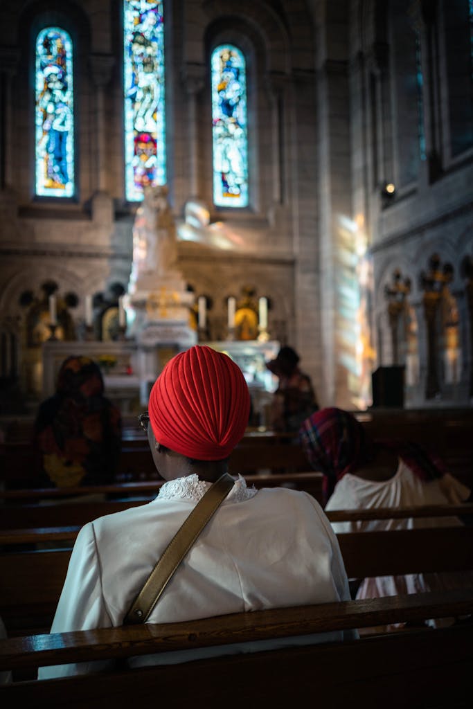 A woman prays peacefully in a Paris church with stained glass windows.