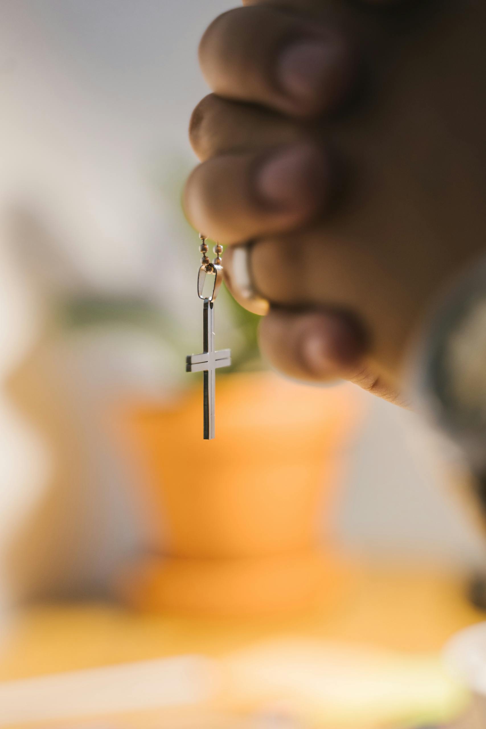 Close-up of hands clasped in prayer holding a cross pendant with blurred background.