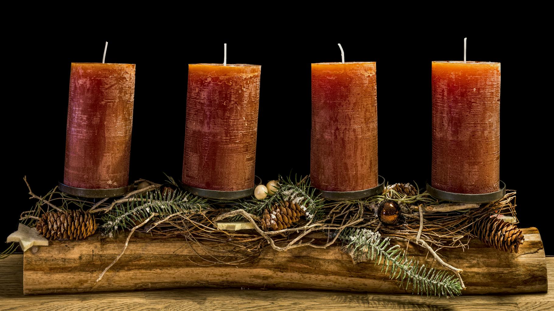 Four rustic advent candles on a wooden display with pine cones and greenery.