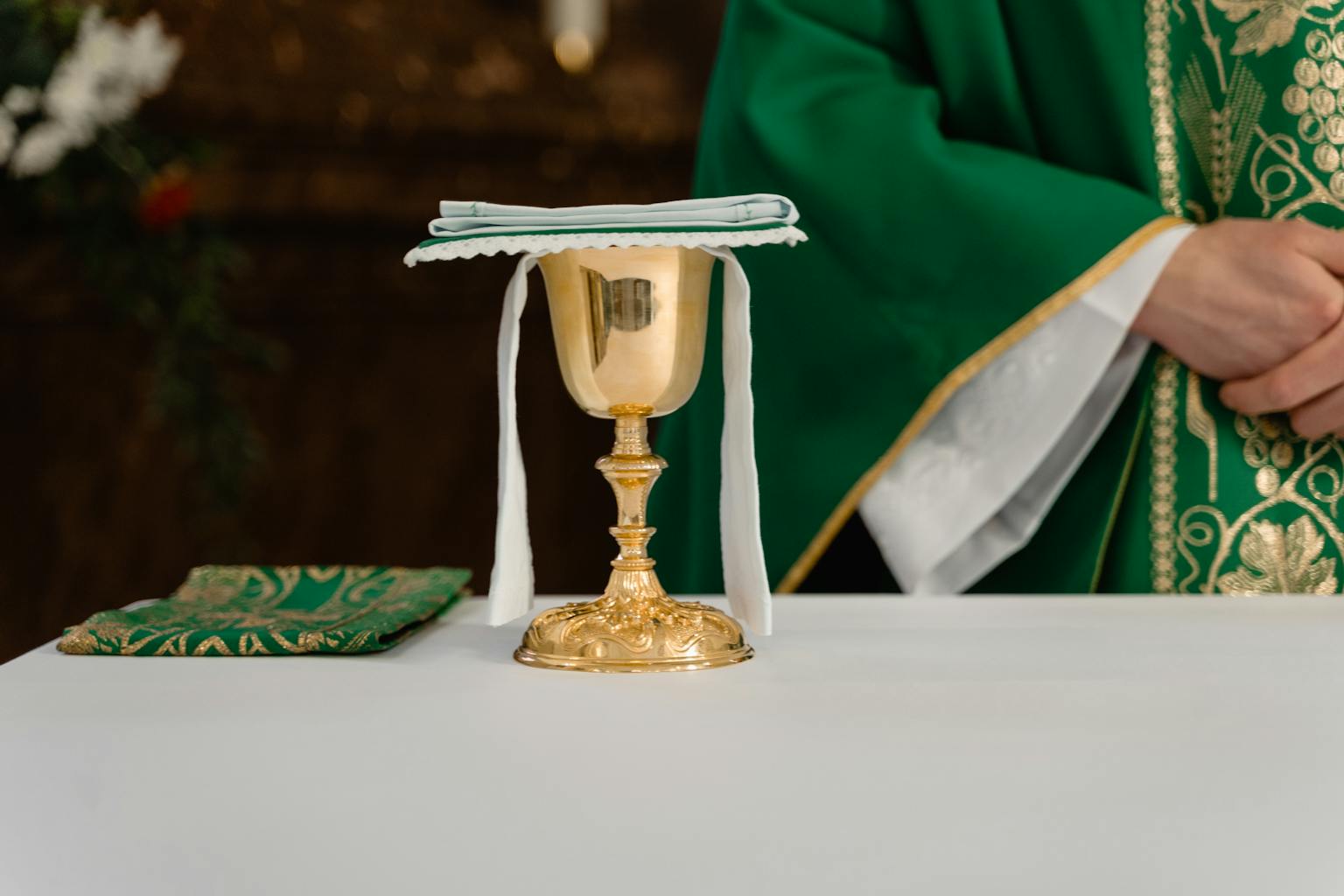 Gold chalice on altar with priest in green robes during a Christian ceremony.