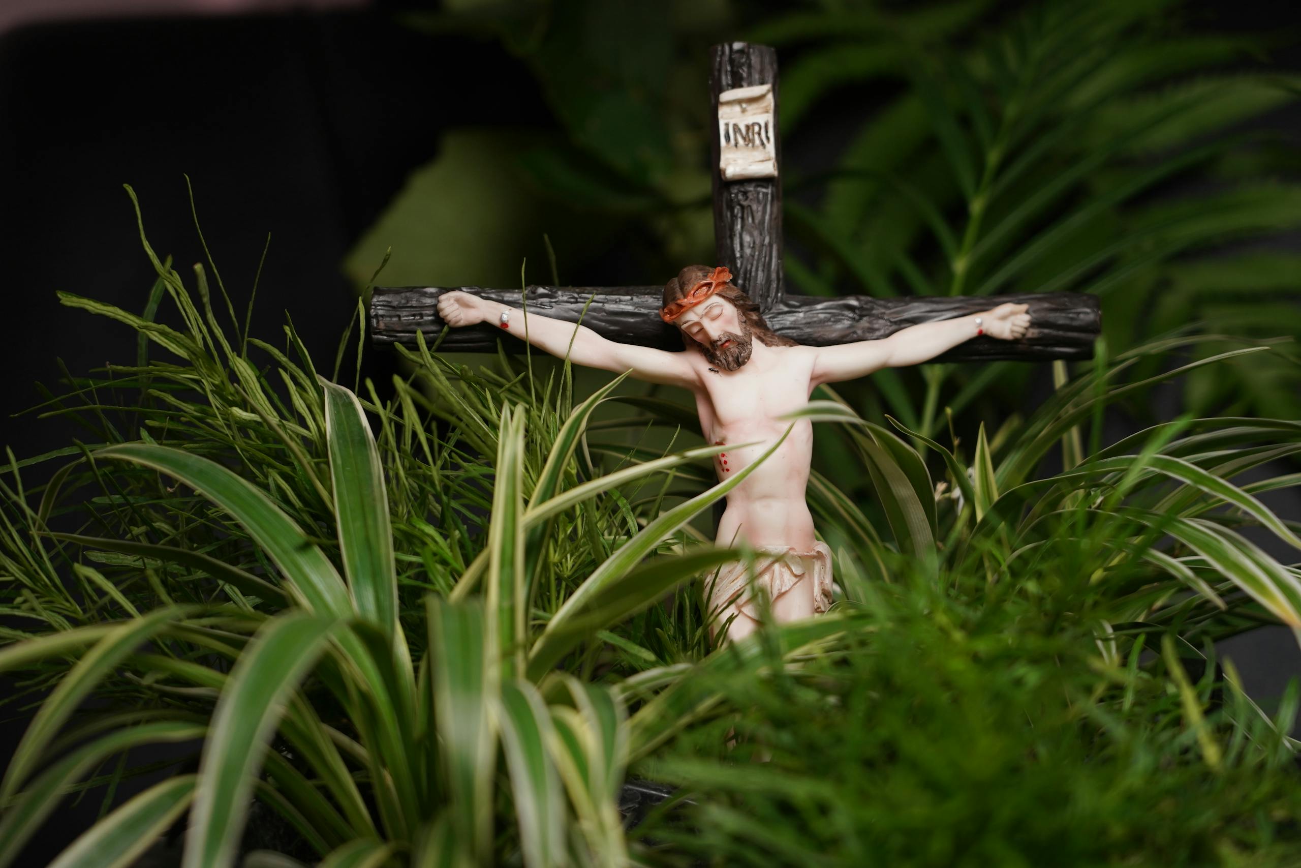 Close-up of a crucifixion sculpture featuring Jesus Christ surrounded by green foliage.