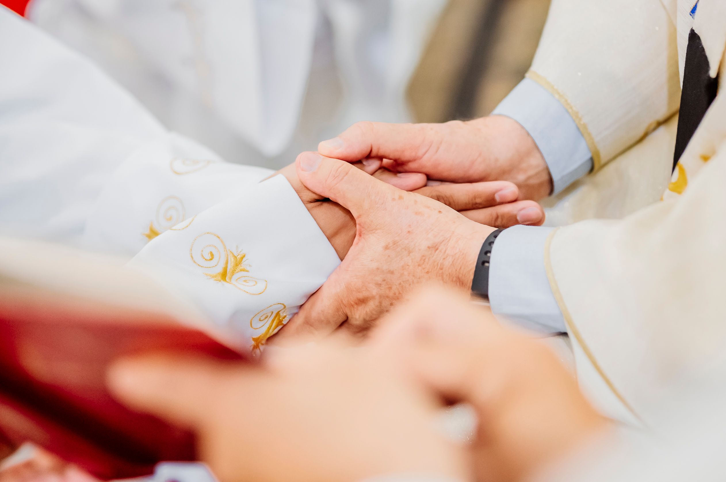 Close-up image of priests holding hands in a religious ceremony, expressing faith and unity.